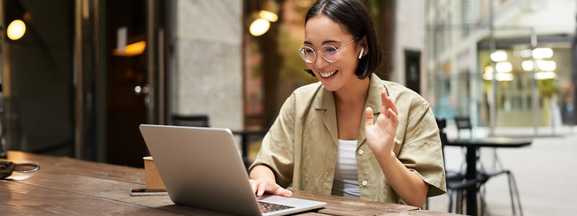 Mulher sorrindo em videochamada no notebook, sentada em uma mesa de café