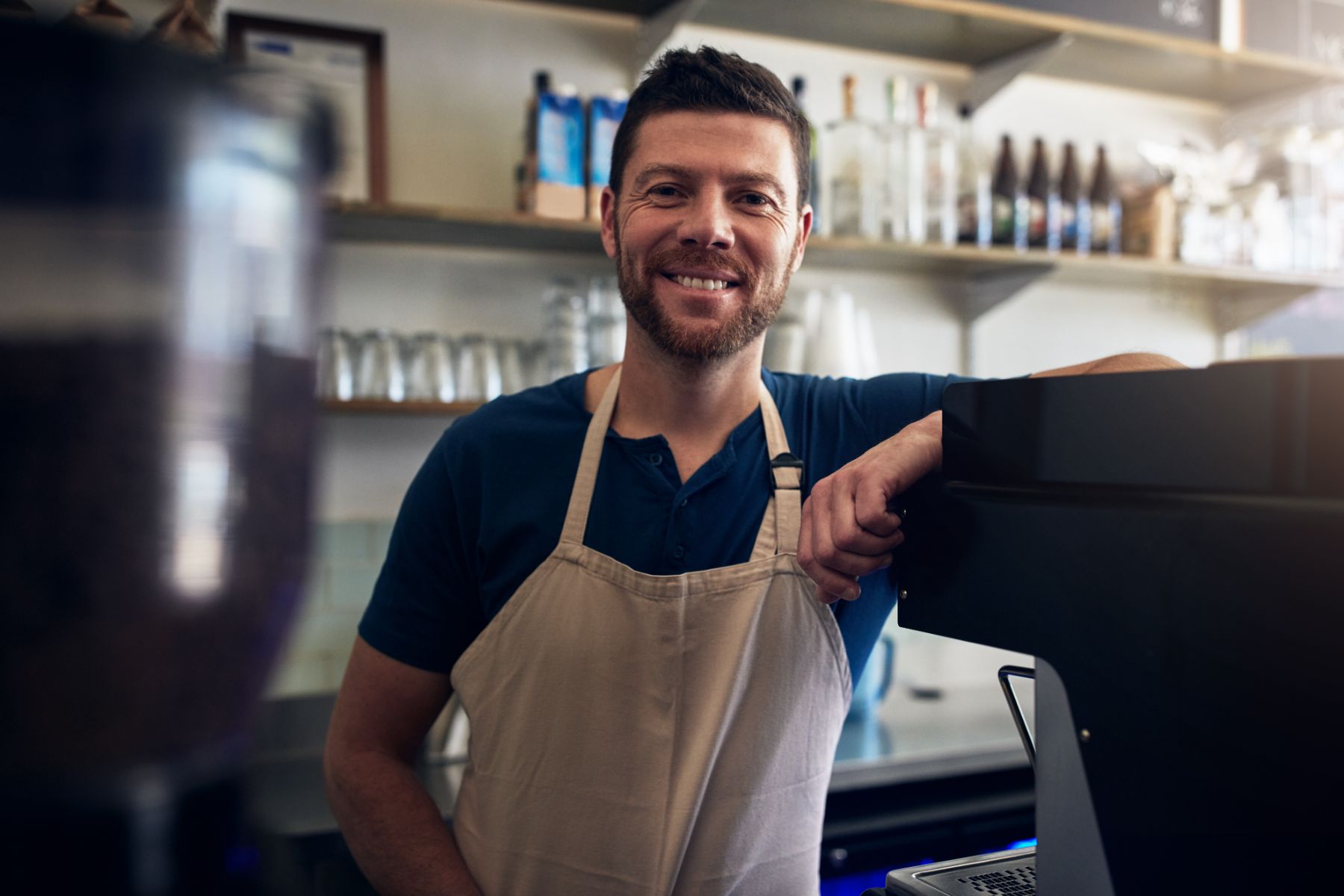 Barista sorrindo apoiado na máquina de café do balcão